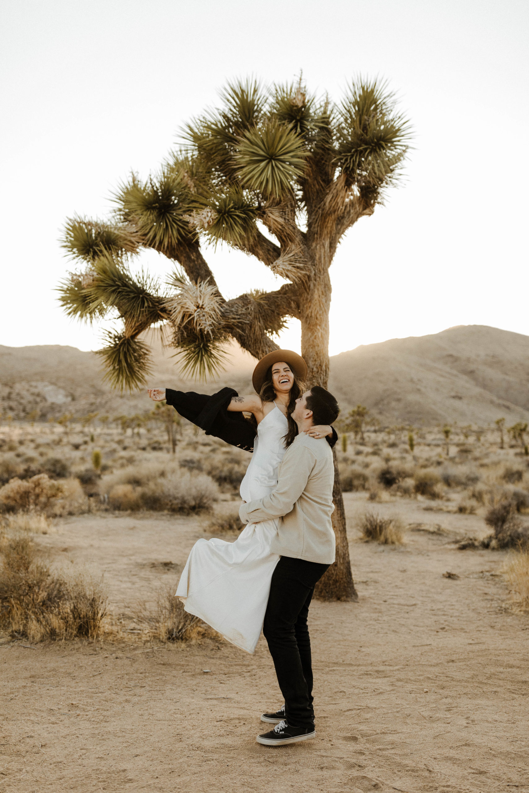 joshua tree elopement couple stands in front of a joshua tree in wedding attire very happy and giggly